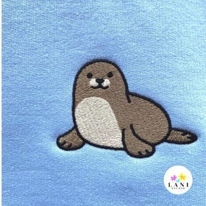 May include: Embroidered seal design in brown, tan, and black on a light blue fabric. The seal is lying down with its flippers extended. The design is from Lani Studio.