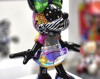 Op de afbeelding: Een kleurrijk Minnie Mouse beeldje met een grote groene strik versierd met hartjes. Het beeldje heeft een zwarte kop met sterren en strepen, een gestreepte kraag en een holografische rok. Haar schoenen zijn blauw en zilver gestreept.