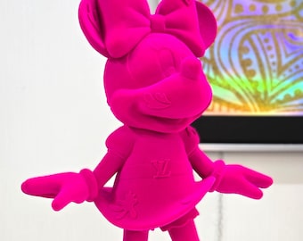 Op de afbeelding: Een felroze beeldje van een cartoonmuis die een jurk en een strik draagt. De muis heeft een groot hoofd en een klein lichaam. De jurk heeft een witte "Y" op de voorkant.