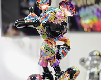 Op de afbeelding: Een glanzend Mickey Mouse beeldje in pop-art stijl. Het zwarte beeld is versierd met levendige stripboekafbeeldingen, met woorden als "LOL!" en "BANG!" op de oren, korte broek en schoenen. Het staat op een zwart-wit gespikkelde basis.