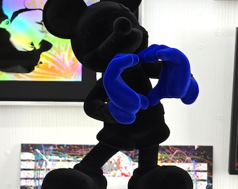 Op de afbeelding: Een zwart fluwelen Mickey Mouse-beeldje dat een hartvorm maakt met zijn handen. De handen zijn felblauw.