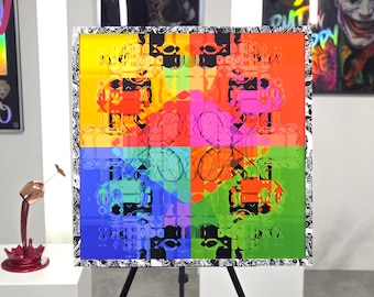 Op de afbeelding: Een pop-art canvas print met een herhalend robotontwerp in vier levendige kleurblokken: rood, roze, groen en blauw. Het kunstwerk heeft een zwart-wit patroonrand en wordt tentoongesteld op een zwart schildersezel.