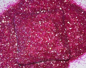 May include: A pile of pink glitter with iridescent shimmer. The glitter is loose and scattered on a white surface.