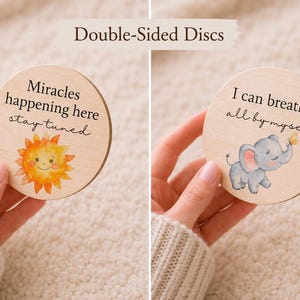 May include: Two wooden discs with inspirational quotes and illustrations. One disc features a smiling sun and the text "Miracles happening here stay tuned." The other shows a gray elephant and the text "I can breathe all by myself."