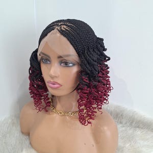 Puede incluir: Una peluca trenzada negra con puntas rizadas burdeos se muestra en una cabeza de maniquí. La peluca presenta una parte delantera de encaje y está peinada con un collar de cadena dorada. El maniquí está sobre un fondo blanco.