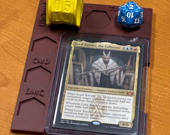 May include: A burgundy card game organizer with a yellow life counter, a blue die, and a card featuring "Lord Xander, the Collector." The organizer has slots for cards and dice, with "CMD" and "DMG" labels.