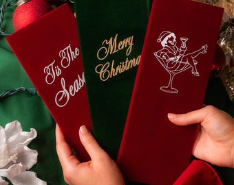 May include: Three rectangular velvet cards in deep red and forest green. One red card features white text reading Tis The Season, one green card has gold text reading Merry Christmas, and one red card displays a white graphic of a person in a martini glass.