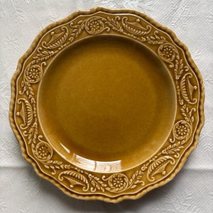 May include: A brown ceramic dinner plate with a decorative, raised, floral design around the rim.