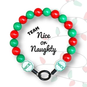 May include: Red and green beaded bracelet with a black metal clasp. The bracelet has two white tags that say "NICE" in green letters. The text "TEAM Nice or Naughty" is written in black cursive on a white background.