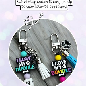 May include: Two keychains with swivel clasps. Each keychain has a charm that reads "I LOVE MY DOODLE" in rainbow colors, a paw print, and a bone. One has a white tassel, the other a blue tassel.