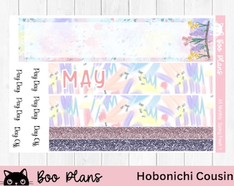 May include: A planner sticker sheet in pastel shades. The word "MAY" is in the centre, with "Pay Day" and "Day Off" labels. The design features watercolour brushstrokes, glitter stripes, and floral accents. The text "Boo Plans" and "Hobonichi Cousin" are also visible.