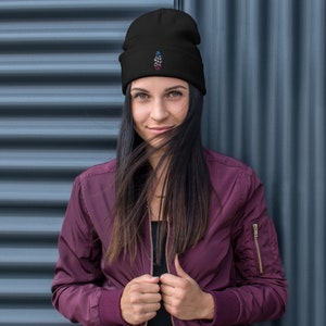 Peut inclure: Un bonnet noir avec du texte brodé en bleu, blanc et rouge. Le bonnet est fait d'une matière douce et est porté par une personne. L'arrière-plan est un métal ondulé gris foncé.