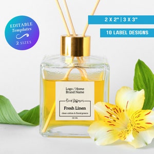 Op de afbeelding: Een doorzichtige glazen fles met een gouden dop en houten stokjes, gevuld met een gele vloeistof. De fles heeft een etiket met de tekst "Logo / Home Brand Name -Reed Diffuser- Fresh Linen clean cotton & floral greens OZ ML".
