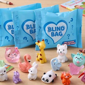May include: Three light blue plastic blind bags with white heart graphics and the text BLIND BAG, accompanied by a collection of miniature animal figurines including a yellow giraffe, white dog, pink flamingo, panda, and various other colorful creatures.