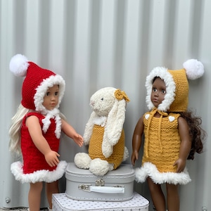 Könnte beinhalten: Zwei Puppen in gestrickten Kleidern und Mützen, eine in Rot und eine in Gelb, mit einem weißen Plüschkaninchen in einem gelben Kleid. Die Puppen stehen auf zwei Vintage-Koffern mit weißen Sternen.