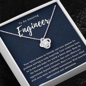 May include: A silver necklace with a knot-shaped pendant, featuring a central clear stone and smaller surrounding stones. The necklace is displayed on a navy blue card with the text "To An Amazing Engineer".