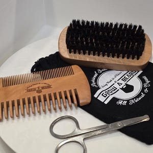 May include: A grooming kit featuring a wooden beard brush, a wooden comb, and small silver scissors. The kit includes a black bag with the text "GROW A BEARD" and "All Natural". The brush is approximately 13 cm long.