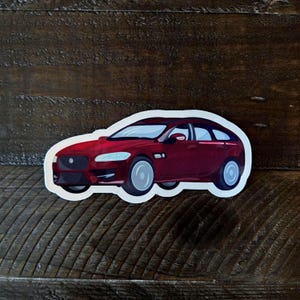 Puede incluir: Adhesivo de un coche familiar de color granate con ruedas plateadas y contorno blanco. La ilustración está sobre una superficie de madera oscura.