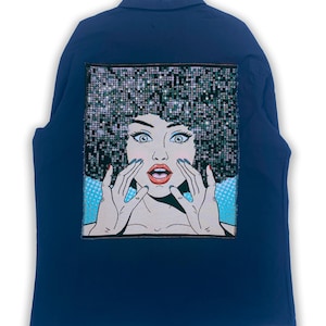 Pode incluir: Uma camisa azul marinho de manga comprida com uma imagem de estilo pop art de uma mulher com um afro brilhante, as mãos levantadas para o rosto, e uma expressão de surpresa. A imagem está na parte de trás da camisa.