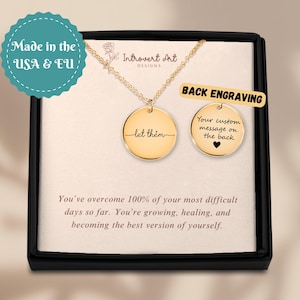 May include: Gold-colored pendant necklace with a round charm that says "let them". A second charm shows a heart and the words "Your custom message on the back". The necklace is displayed in a black box.