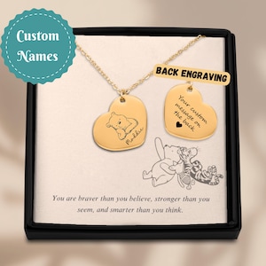 May include: Gold heart pendant necklace with a bear illustration and the name "Maddie." The necklace includes a second heart-shaped pendant with the text "Your custom message on the back." The box reads "You are braver than you believe."