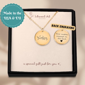 May include: Gold-colored necklace with a round pendant featuring a shark design. The necklace is presented in a black gift box with the text "Back Engraving" and "Your custom message on the back". The box also includes the text "a special gift just for you".