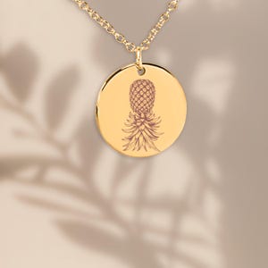 Puede incluir: Collar de oro con un colgante redondo con un diseño de piña grabado en detalle.