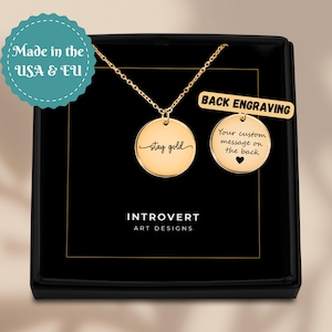 May include: A gold-colored necklace with a round pendant that says "stay gold" in cursive. The necklace is displayed in a black box with the words "INTROVERT ART DESIGNS". A second pendant shows "Your custom message on the back".