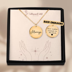 May include: A gold-colored pendant necklace with a round charm that says "Always" in cursive. The necklace is in a black box with a white interior. A second charm shows "Your custom message on the back" with a heart symbol. The text "Back Engraving" is also visible.
