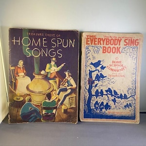 May include: Two vintage songbooks. The left book, "Treasure Chest of Home Spun Songs," has a dark purple cover with illustrations of people singing and playing instruments. The right book, "The Everybody Sing Book," has a light beige cover with blue illustrations of birds.