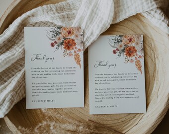 May include: Two thank you cards featuring floral designs in shades of orange, peach, and green. The text on the cards reads "Thank you!" and includes a message expressing gratitude for the presence and generosity of guests at a wedding. The cards are signed "Lauren & Miles".
