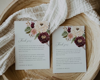 May include: Two thank you cards with floral designs in shades of pink, white, and burgundy. The cards have the text "Thank you!" and "From the bottom of our hearts we would like to thank you for celebrating our special day with us and making it the most memorable day of our lives." The cards are sitting on a wooden surface.