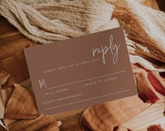May include: A brown RSVP card with white text. The card says "reply" in cursive and "Kindly reply by by April 20th". There are two options to choose from: "Will Attend" and "Unable to Attend". There is also a space for "Dietary Requirements".