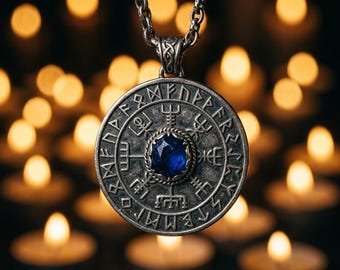 May include: A circular silver-toned pendant featuring an intricate engraved compass design with runic symbols along the outer edge and a faceted deep blue gemstone set in the center, suspended from a matching silver-toned metal chain link necklace.