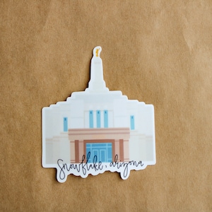 Op de afbeelding: Een witte sticker met een cartoonillustratie van de Snowflake Arizona Tempel. De sticker heeft de tekst "Snowflake, Arizona" in zwarte cursieve letters.