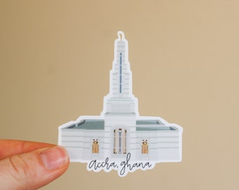 Op de afbeelding: Witte sticker van de Accra Ghana Tempel met de tekst "Accra, Ghana" eronder.