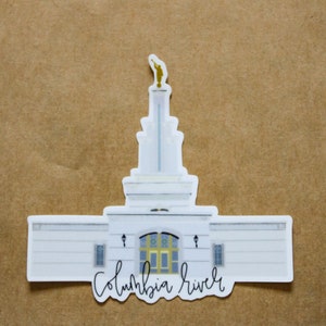 Op de afbeelding: Witte sticker van de Columbia River Tempel met een gouden toren en de tekst "Columbia River" onderaan.