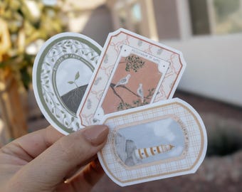 Op de afbeelding: Drie gestanste stickers met decoratieve randen. Een ovale sticker toont een groene kiem met wortels en de tekst "Anchor of Faith". Een rechthoekige sticker toont twee witte vogels op een tak met "Messenger of Hope". Een derde sticker toont een vuurtoren.