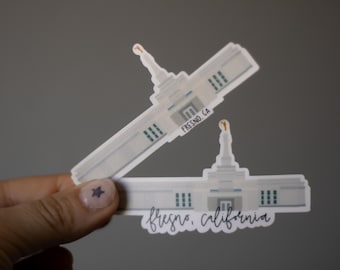 May include: Two white stickers of a building with a spire, windows, and a doorway. One sticker has the text "FRESNO, CA" and the other says "fresno, california" in cursive. The stickers are held against a gray background.