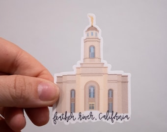 May include: A sticker featuring a beige building with a tall tower and arched windows. The sticker has the text "feather river, California" in a script font. A gold statue is on top of the tower.