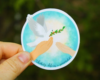 May include: A white dove with an olive branch in its beak flies towards two outstretched hands. The background is a blue and white watercolor wash with the text "Charity defines a peacemaker".
