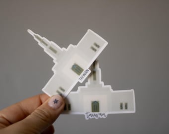 May include: Two white stickers featuring a building design with the word "Taiwan" printed on them. The stickers have a light green door and window accents. One sticker is positioned on top of the other.