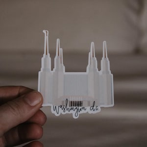 Op de afbeelding: Witte sticker van een kerkgebouw met de tekst "Washington D.C." eronder.