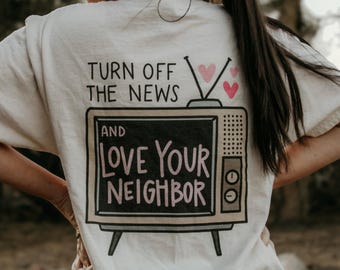 May include: White t-shirt with a graphic of a vintage television with the text "Turn off the news and love your neighbor" and three pink hearts.