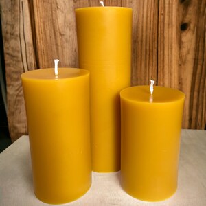 May include: Three yellow beeswax candles of different sizes. The candles are cylindrical and have a smooth, matte finish.