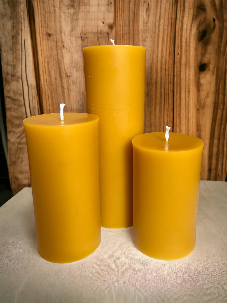 May include: Three yellow beeswax candles of different sizes. The candles are cylindrical and have a smooth, matte finish.