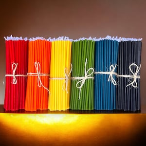 May include: A bundle of colorful beeswax candles tied with twine. The candles are arranged in a rainbow pattern, with red, orange, yellow, green, blue, and black candles.