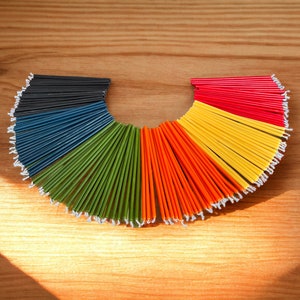 May include: A semi-circular arrangement of colorful candles. The candles are fanned out, displaying a spectrum of colors including black, blue, green, orange, yellow, and red. The candles are on a wooden surface.