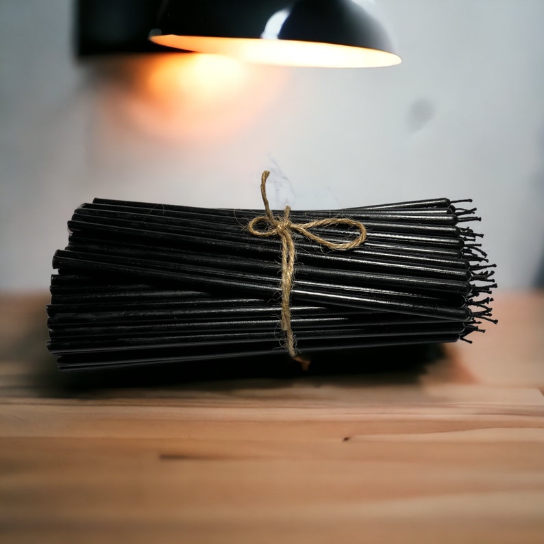 May include: A bundle of black taper candles tied together with twine. The candles are arranged in a neat stack and are ready to be used.