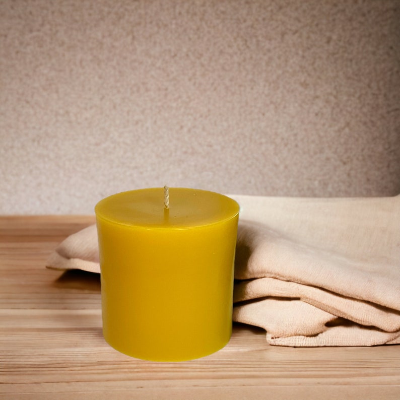 May include: A yellow pillar candle on a wooden surface with a beige fabric folded behind it.